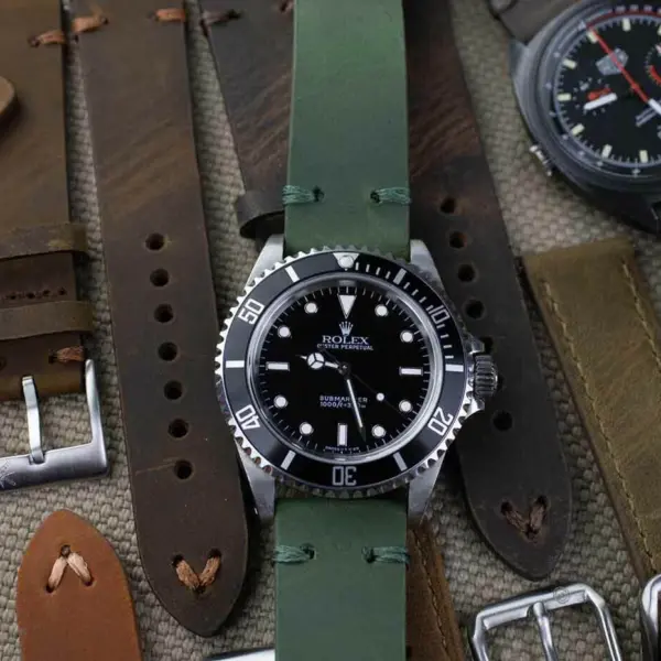 A collection of classic watch bracelets for men, featuring various styles and colors, including green and brown leather straps, displayed alongside a black dive watch