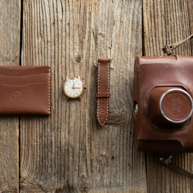 Close-up of leather wallet, watch, and camera case on wooden surface.