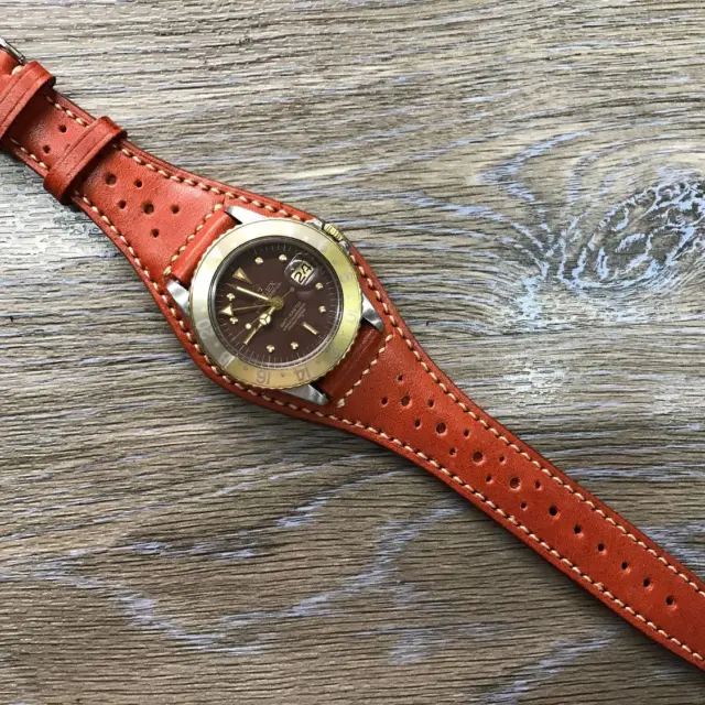 A close-up of a stylish cuff watch strap in orange leather with perforations, featuring a round brown watch face, set against a wooden background