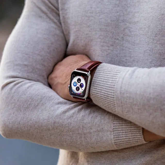 A close-up of a person's arm crossed over their chest, showcasing a stylish watch with a brown strap against a neutral sweater background. Perfect for unique watch strap styling tips